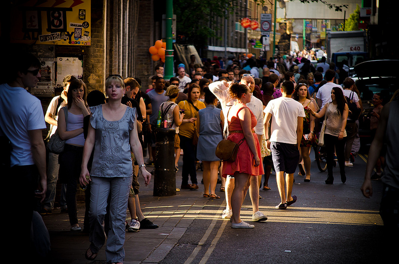 L'immagine mostra un mercato a Brick Lane, nel quartiere di Shoreditch, a Londra. Il mercato si svolge il sabato e la domenica e vende una varietà di articoli, tra cui cibo, vestiti, accessori e oggetti d'antiquariato. La strada è fiancheggiata da bancarelle colorate e c'è un grande afflusso di persone. L'atmosfera è vivace e movimentata e l'immagine cattura l'essenza del mercato.