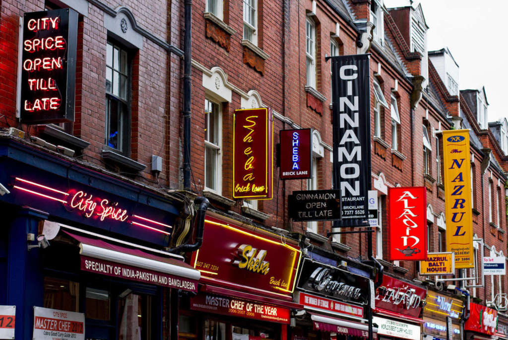 La foto mostra alcuni edifici di Brick Lane. La strada è fiancheggiata da edifici bassi e colorati.