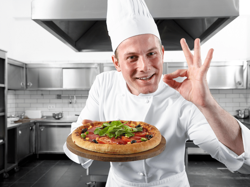In questa immagine viene mostrato un pizzaiolo a Londra che mostra in primo piano una pizza appena realizzata.