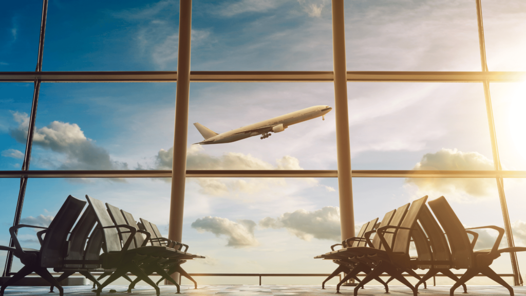 Immagine puramente decorativa. Mostra la sala di attesa agli imbarchi vuota e sullo sfondo un aereo bianco che decolla.